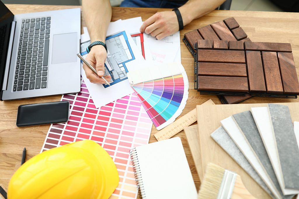 Top view of interior designer looking through construction of new house building. Wooden samples on desktop. Silver pen in hand. Colourful palette and laptop on working table. Renovation concept