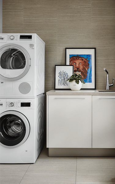 Neat and organised, the laundry area comprises cabinetry by Mudian, a large sink with under counter storage, a wet wash area, stacked washer and dryer, and Caesarstone countertops.