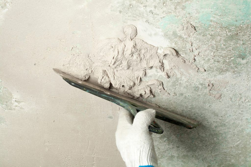 Worker with spatula and concrete cement plaster on grey wall background, top view
