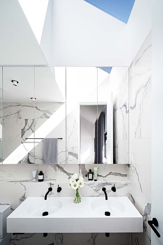 Mirrored cabinets in this bathroom reflect the marble pattern of its walls and double the spatial feel of the space.