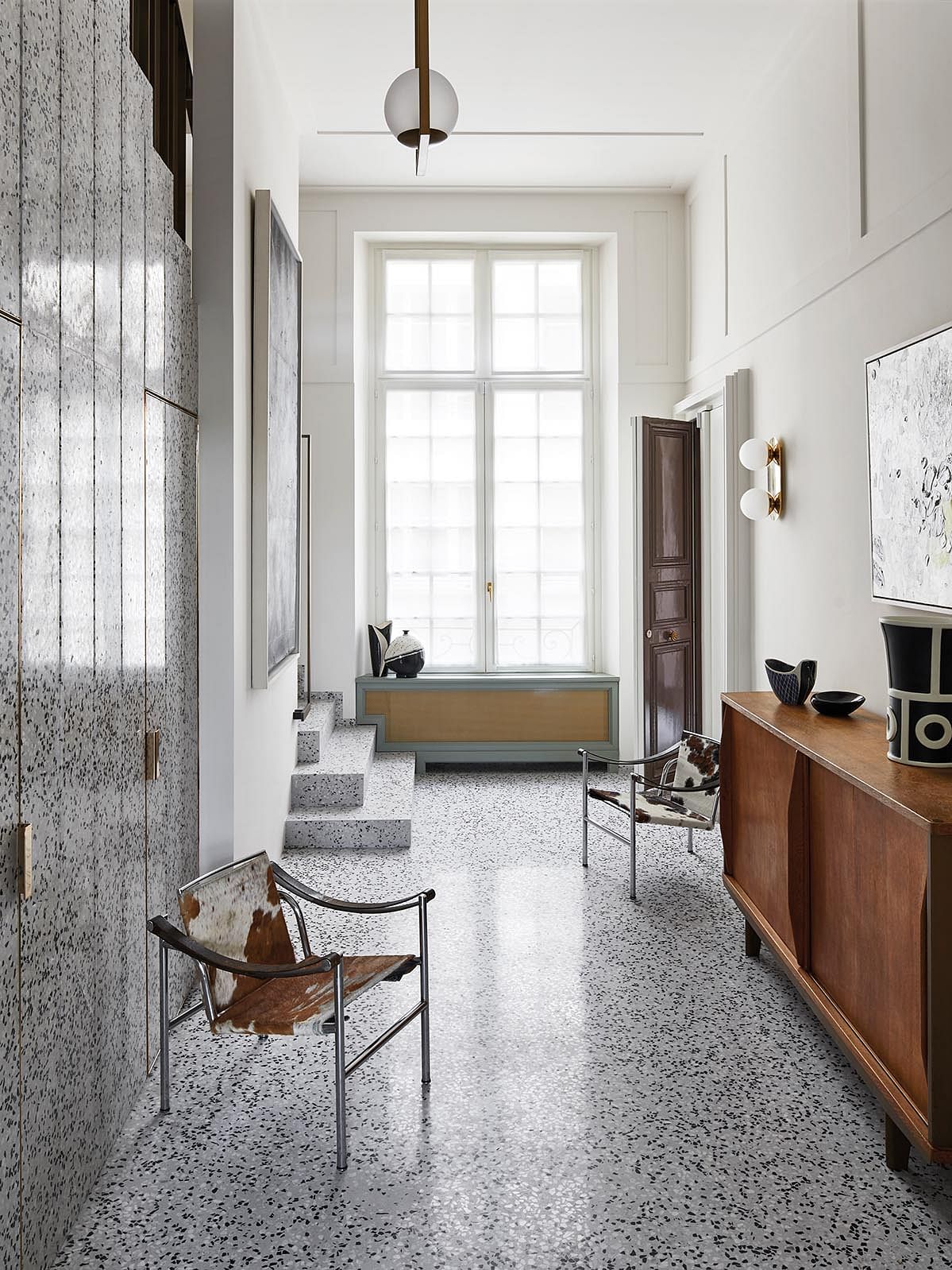 The hallway is a carefully orchestrated composition comprising Le Corbusier Sling chairs (1950), a Jean Prouvé chest, Subway drawings by Keith Haring and ceramics by Georges Jouve and Olivier Gagnère against a terrazzo floor.