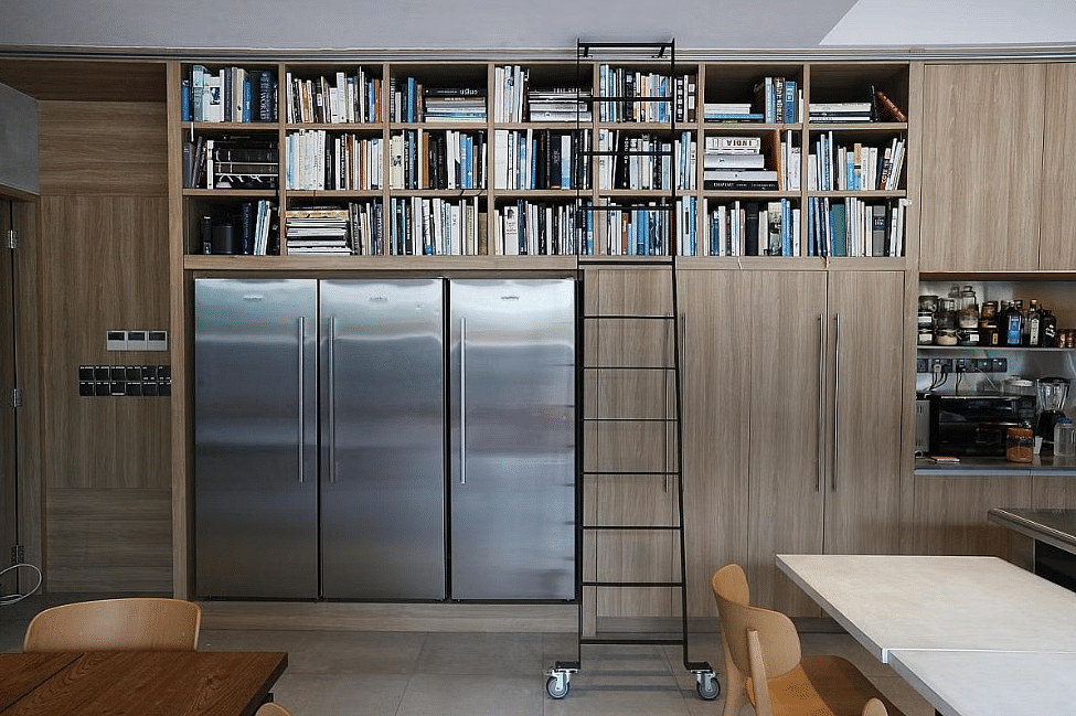Wood panelling and cookbooks placed on shelves above three fridges.