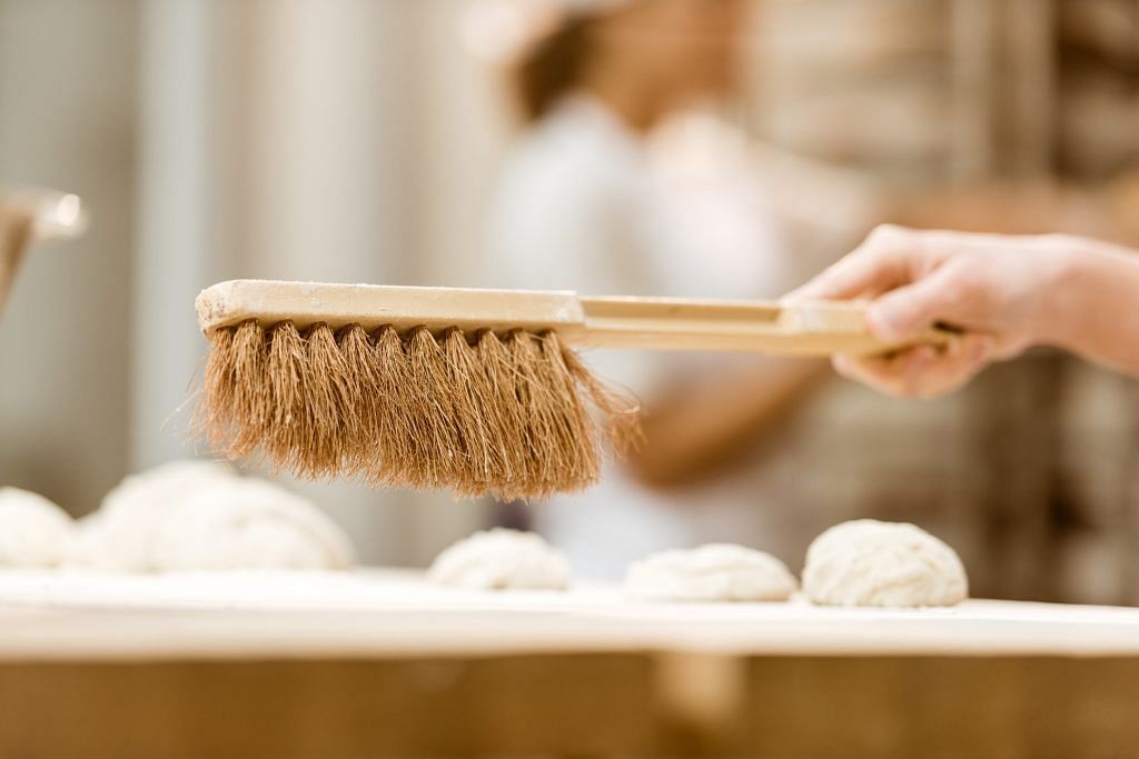 close-up shot of baker cleaning workplace from flour with brush at baking manufacture